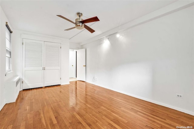 unfurnished bedroom with a closet, rail lighting, light hardwood / wood-style floors, and ceiling fan