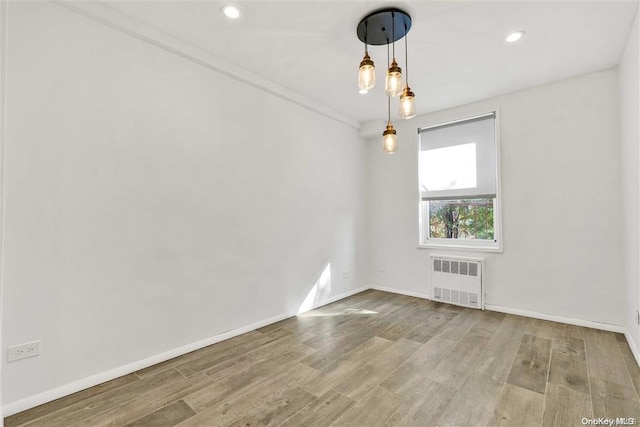 empty room with crown molding, radiator heating unit, and wood-type flooring