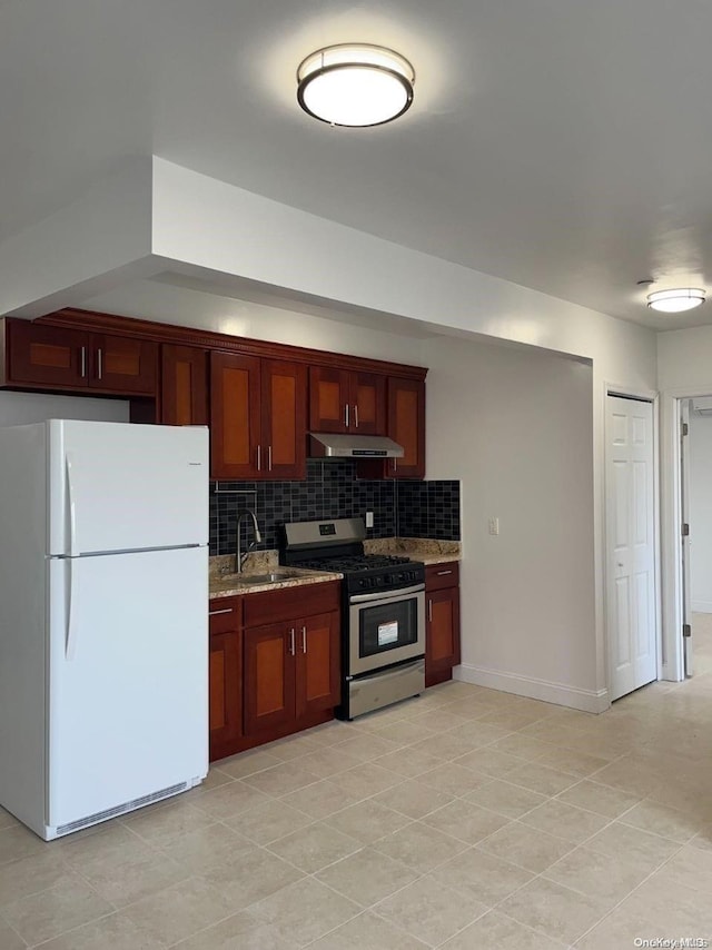 kitchen with light stone countertops, tasteful backsplash, stainless steel gas range, white refrigerator, and light tile patterned flooring