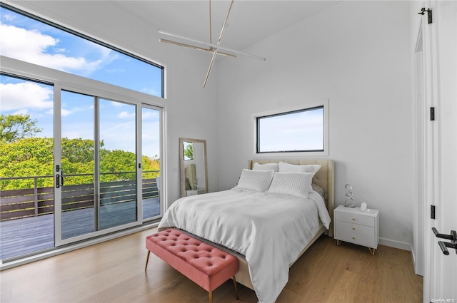 bedroom with access to exterior, light wood-type flooring, a high ceiling, and multiple windows