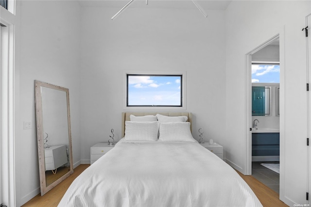 bedroom with ensuite bathroom, light hardwood / wood-style flooring, and multiple windows