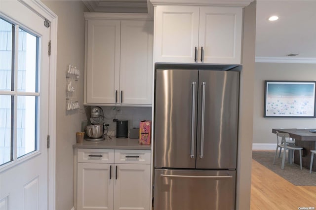 kitchen with stainless steel fridge, backsplash, crown molding, light hardwood / wood-style flooring, and white cabinets