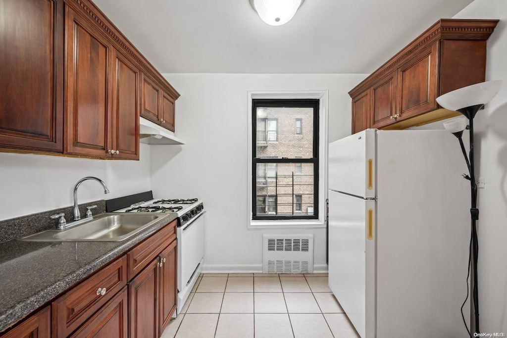 kitchen featuring radiator, sink, dark stone counters, white appliances, and light tile patterned floors