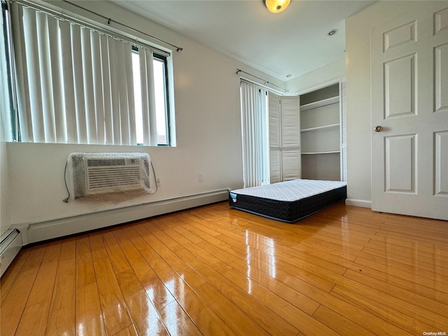 unfurnished bedroom with a wall mounted AC, a baseboard radiator, and light wood-type flooring