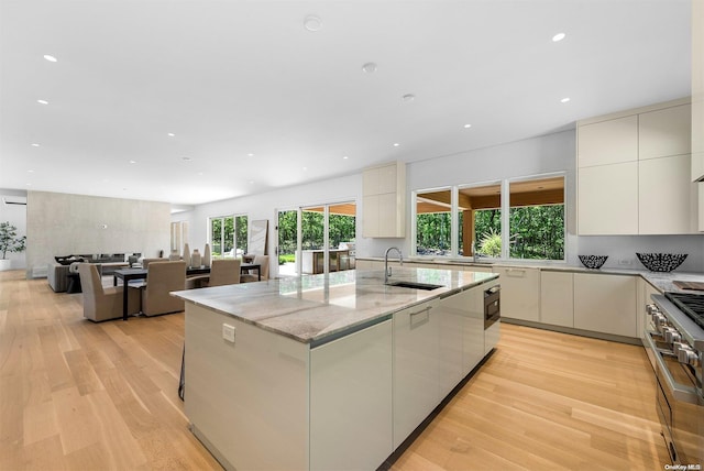 kitchen with light hardwood / wood-style floors, sink, stainless steel range, and an island with sink