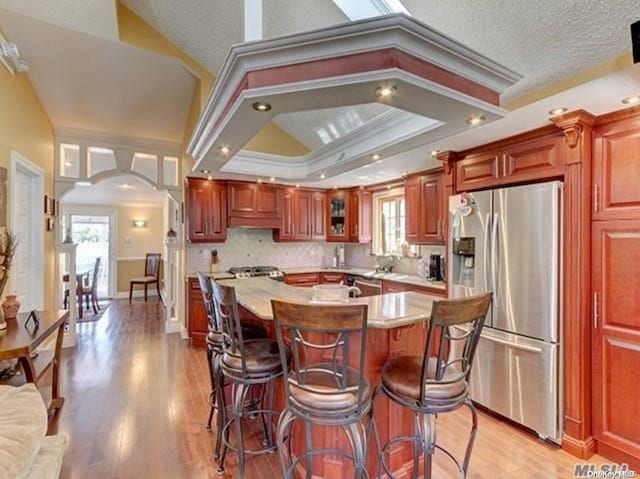 kitchen with stainless steel appliances, light hardwood / wood-style flooring, a tray ceiling, a kitchen bar, and ornamental molding