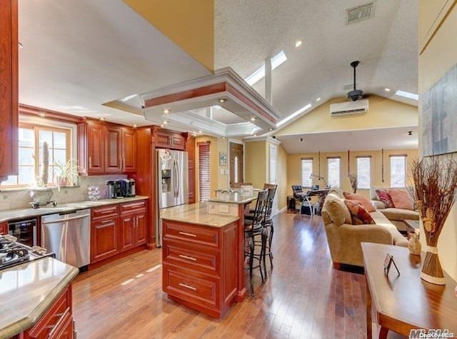 kitchen featuring a center island, stainless steel appliances, light hardwood / wood-style flooring, vaulted ceiling, and a kitchen bar