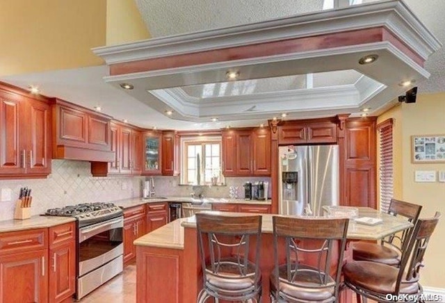 kitchen with appliances with stainless steel finishes, a kitchen island, a raised ceiling, and crown molding