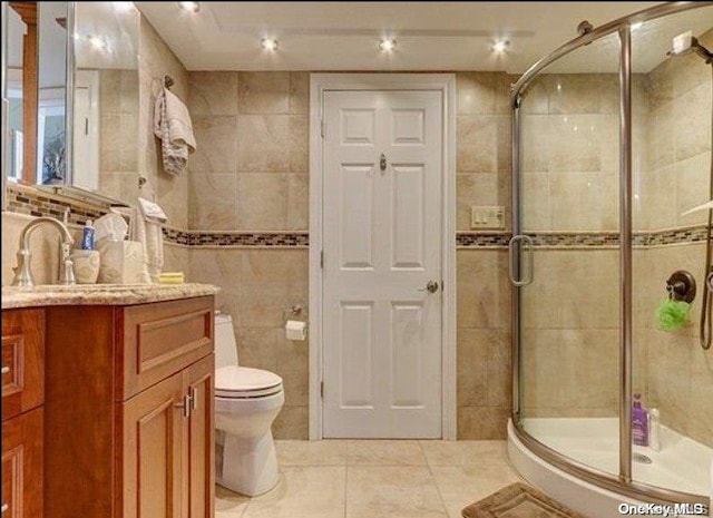 bathroom featuring vanity, tile patterned floors, toilet, tile walls, and an enclosed shower