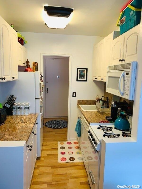 kitchen featuring white cabinetry, sink, light hardwood / wood-style floors, and white appliances