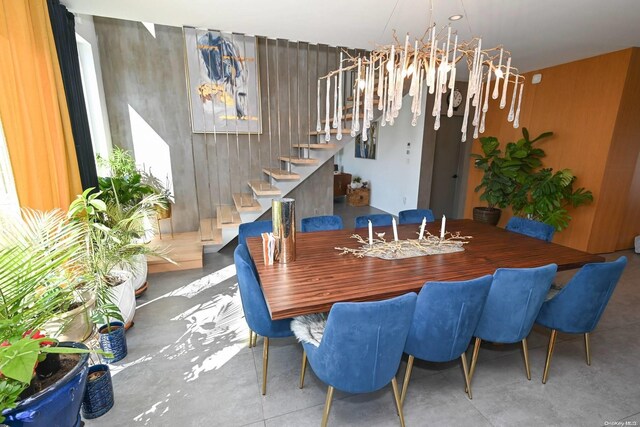 dining area featuring wood walls, concrete flooring, and a notable chandelier