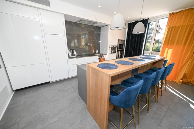 kitchen featuring white cabinets, pendant lighting, a breakfast bar, and an island with sink