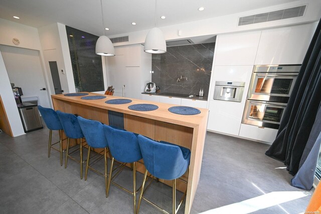 kitchen featuring stainless steel double oven, hanging light fixtures, backsplash, a breakfast bar, and white cabinets