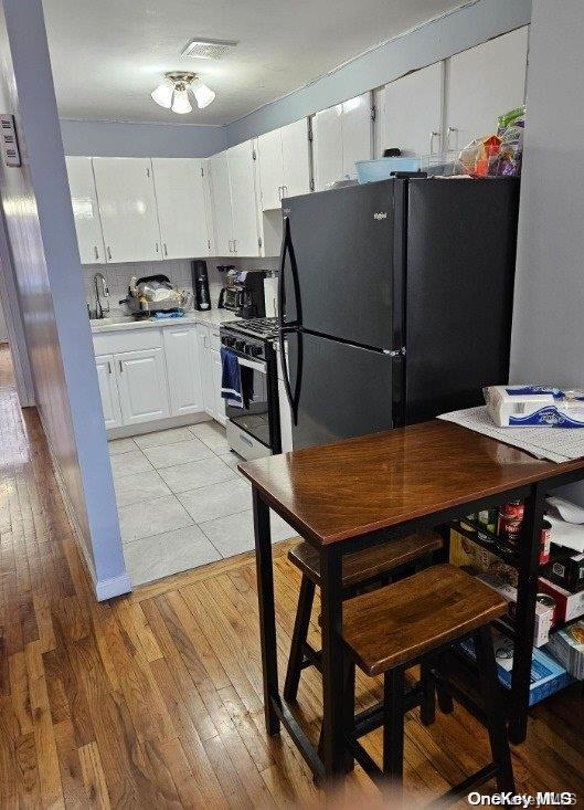 kitchen with black refrigerator, white cabinetry, light hardwood / wood-style flooring, and stainless steel range oven