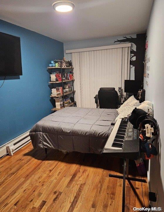 bedroom featuring a baseboard heating unit and hardwood / wood-style flooring