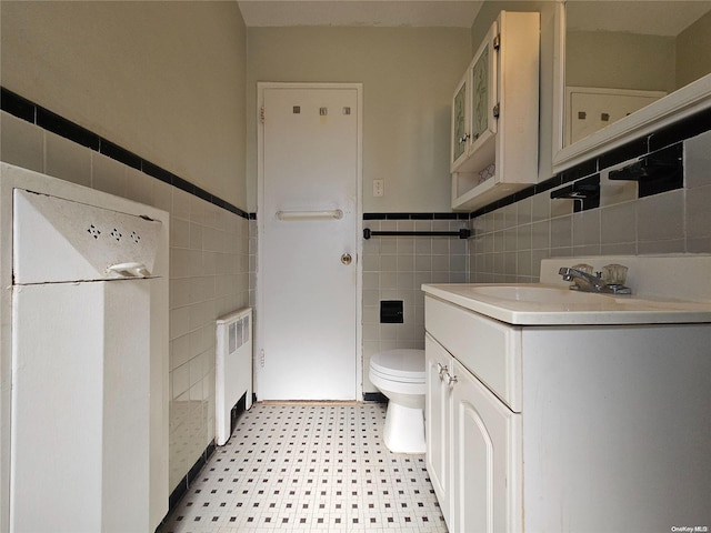 bathroom featuring vanity, toilet, tile walls, and radiator