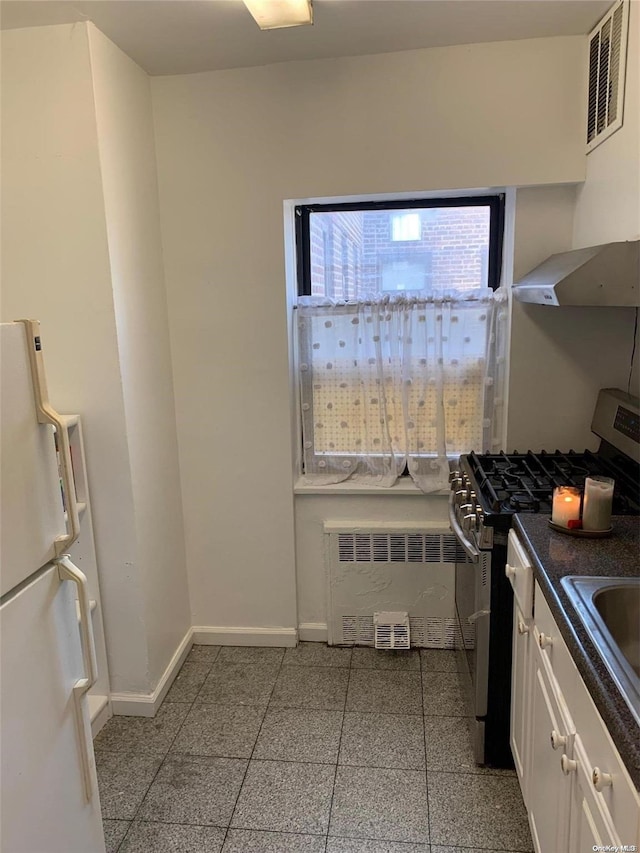 kitchen featuring radiator, white cabinetry, white fridge, extractor fan, and stainless steel range with gas stovetop