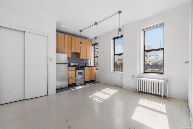 kitchen featuring radiator, hanging light fixtures, appliances with stainless steel finishes, tasteful backsplash, and light hardwood / wood-style floors