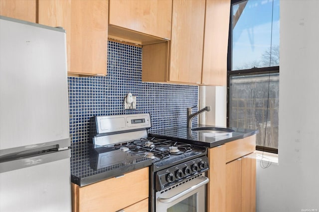 kitchen with sink, backsplash, white fridge, light brown cabinetry, and stainless steel range with gas stovetop