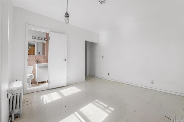 unfurnished bedroom with light hardwood / wood-style floors, radiator heating unit, and ensuite bath