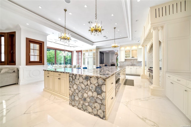 kitchen featuring backsplash, a spacious island, ornate columns, cream cabinetry, and decorative light fixtures