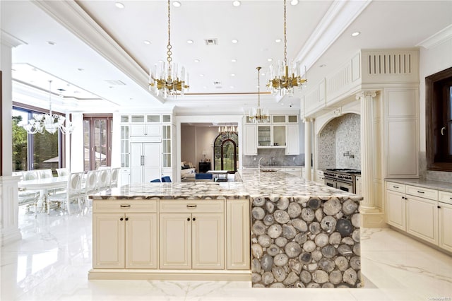 kitchen featuring tasteful backsplash, light stone counters, a large island with sink, cream cabinets, and hanging light fixtures