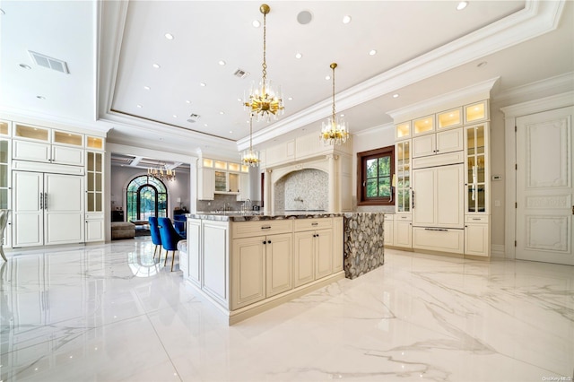 kitchen with pendant lighting, backsplash, cream cabinets, a raised ceiling, and crown molding