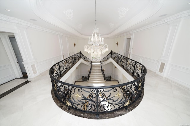 staircase with a raised ceiling, crown molding, and decorative columns