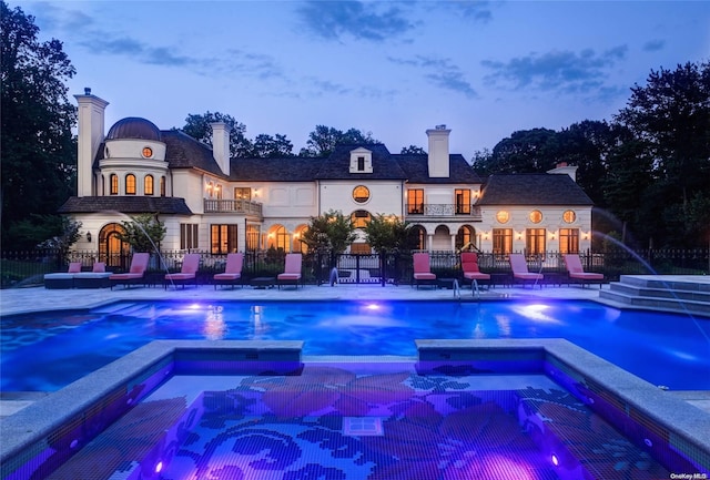 pool at dusk featuring an in ground hot tub, pool water feature, and a patio