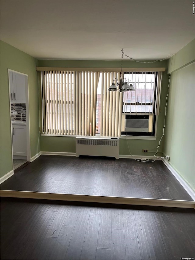 spare room featuring radiator, cooling unit, dark wood-type flooring, and an inviting chandelier