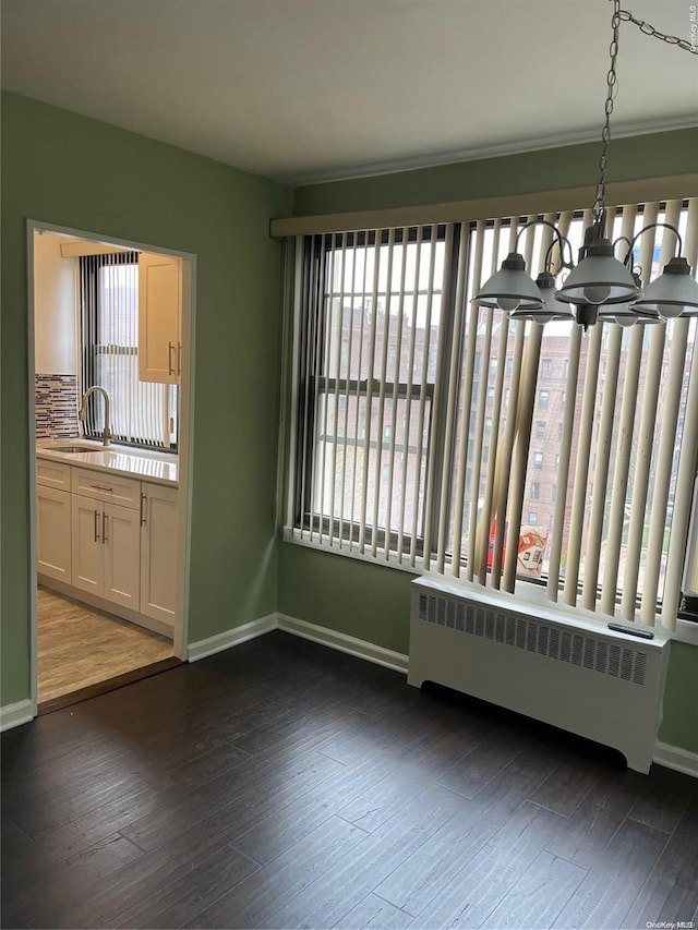 unfurnished dining area featuring dark hardwood / wood-style floors, an inviting chandelier, radiator, and sink