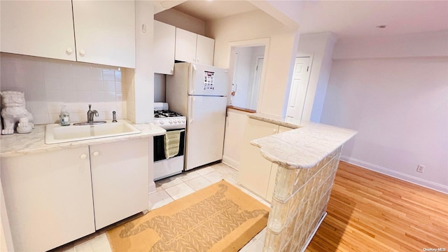 kitchen with sink, backsplash, white appliances, white cabinets, and light wood-type flooring