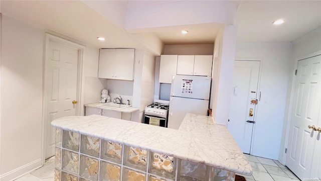 kitchen with white refrigerator, sink, gas range, white cabinetry, and kitchen peninsula