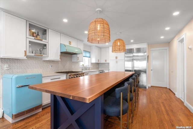 kitchen with a center island, white cabinets, hanging light fixtures, appliances with stainless steel finishes, and wood-type flooring