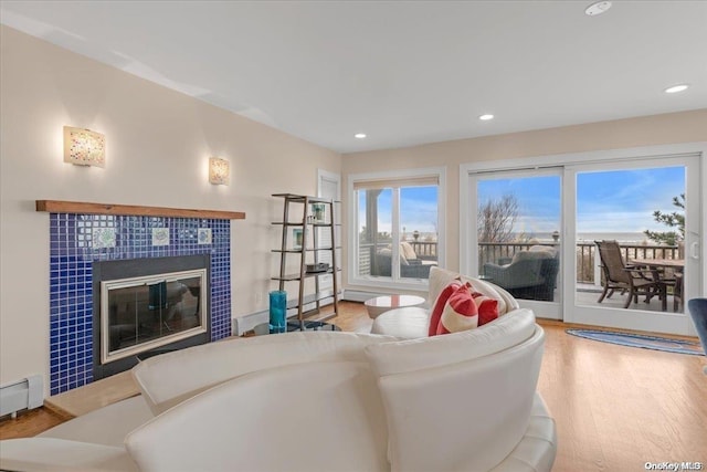 living room with wood-type flooring, a tiled fireplace, and a baseboard heating unit