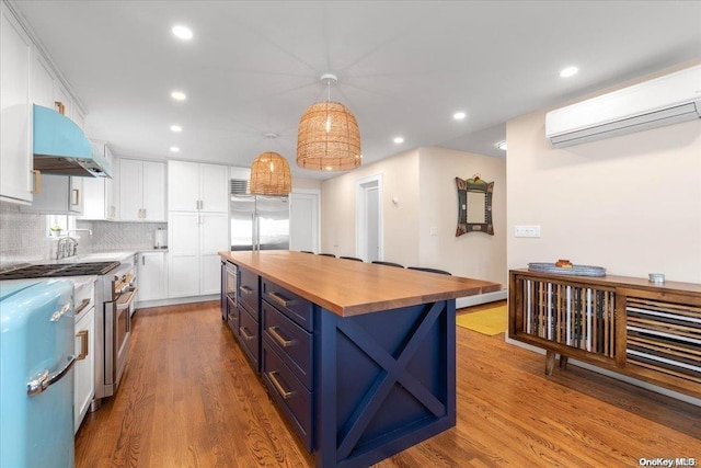 kitchen with white cabinetry, hanging light fixtures, a wall mounted air conditioner, a kitchen island, and built in fridge