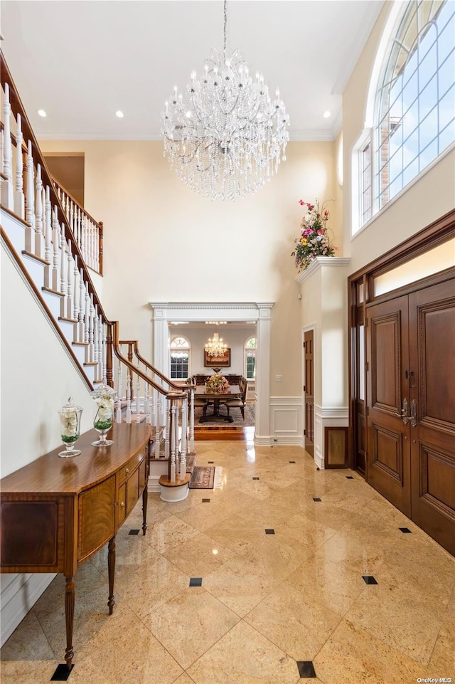 foyer entrance featuring crown molding, a towering ceiling, and an inviting chandelier