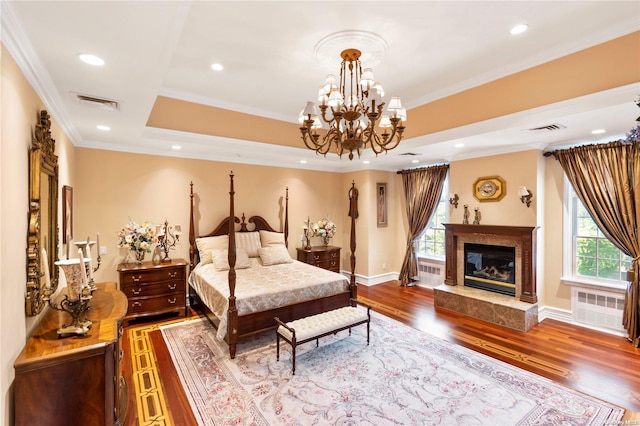 bedroom with radiator, a high end fireplace, a notable chandelier, crown molding, and wood-type flooring