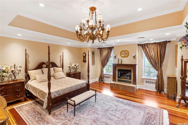 bedroom with a chandelier, ornamental molding, a fireplace, and light hardwood / wood-style flooring