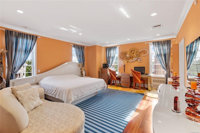 bedroom with radiator heating unit, hardwood / wood-style flooring, multiple windows, and crown molding