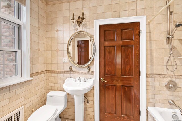 full bathroom featuring tiled shower / bath combo, toilet, tile walls, and sink