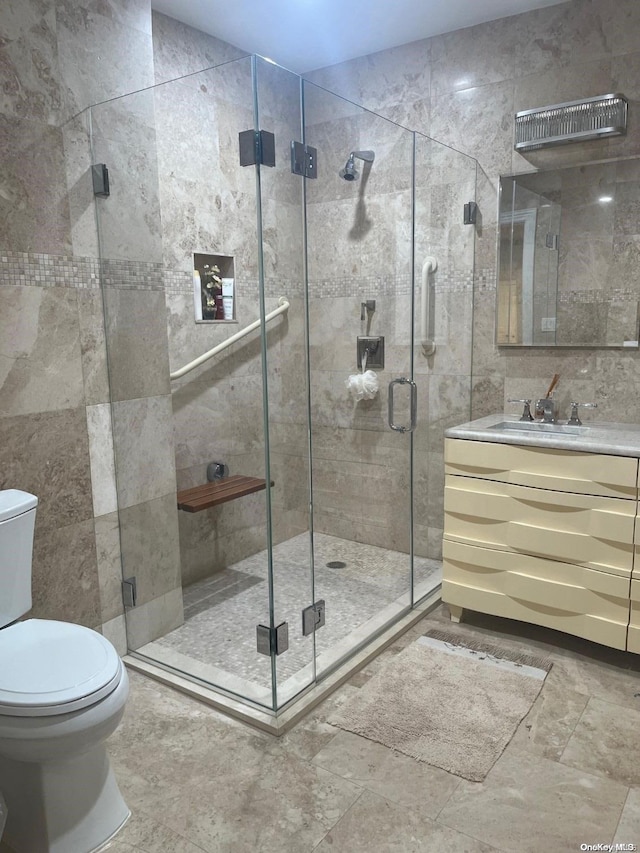 bathroom with vanity, a shower with shower door, tile walls, and toilet