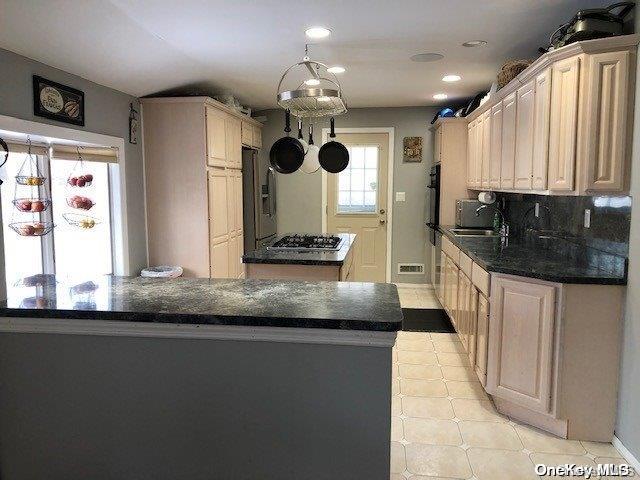 kitchen with baseboards, visible vents, a kitchen island, a sink, and backsplash