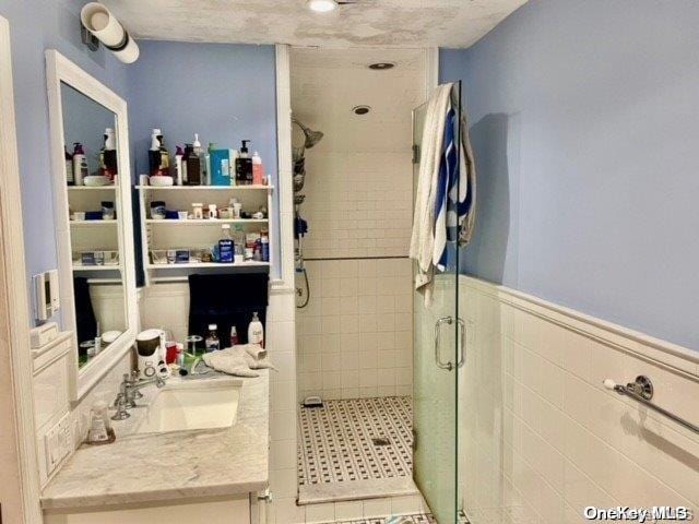 full bathroom with vanity, a shower stall, tile walls, and wainscoting