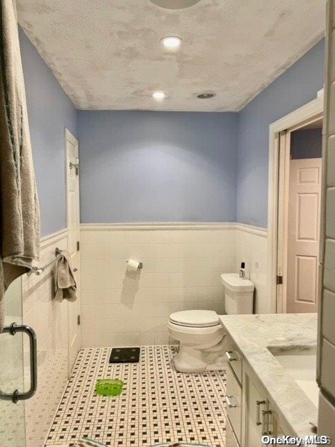 bathroom featuring vanity, toilet, tile patterned flooring, and wainscoting