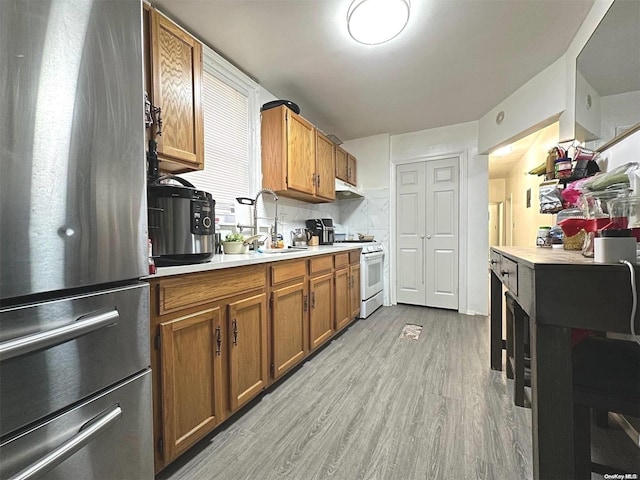 kitchen featuring decorative backsplash, stainless steel fridge, light wood-type flooring, sink, and white stove