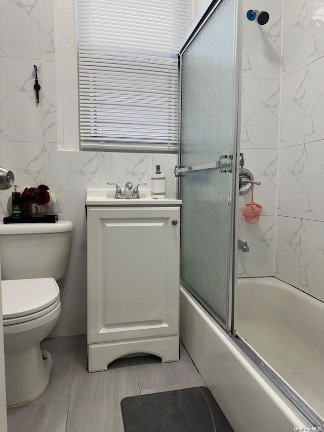 full bathroom with tile patterned floors, toilet, shower / bath combination with glass door, vanity, and tile walls