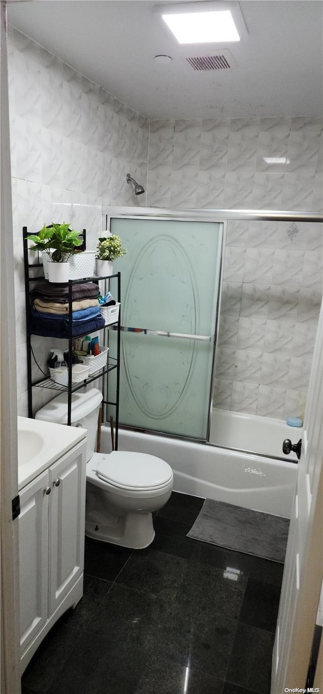 full bathroom featuring toilet, vanity, tile walls, and combined bath / shower with glass door