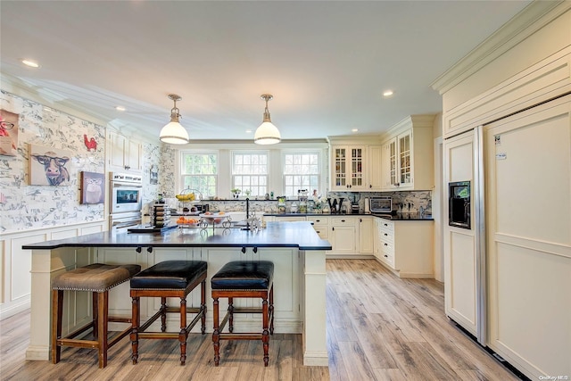 kitchen with a kitchen breakfast bar, light wood-type flooring, stainless steel oven, crown molding, and pendant lighting