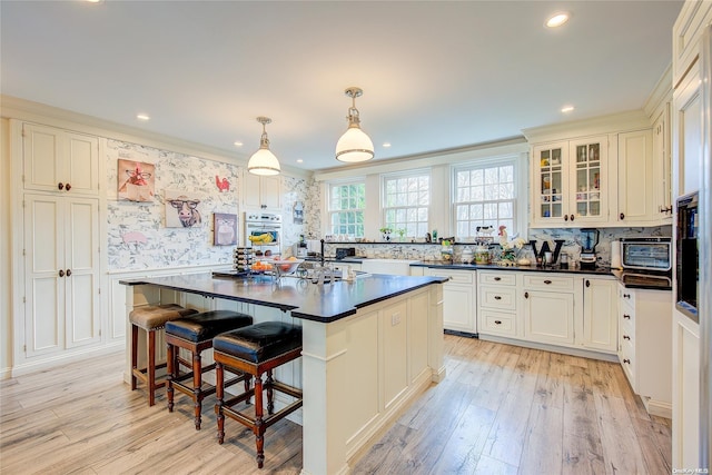 kitchen with a breakfast bar, crown molding, decorative light fixtures, light hardwood / wood-style floors, and a kitchen island